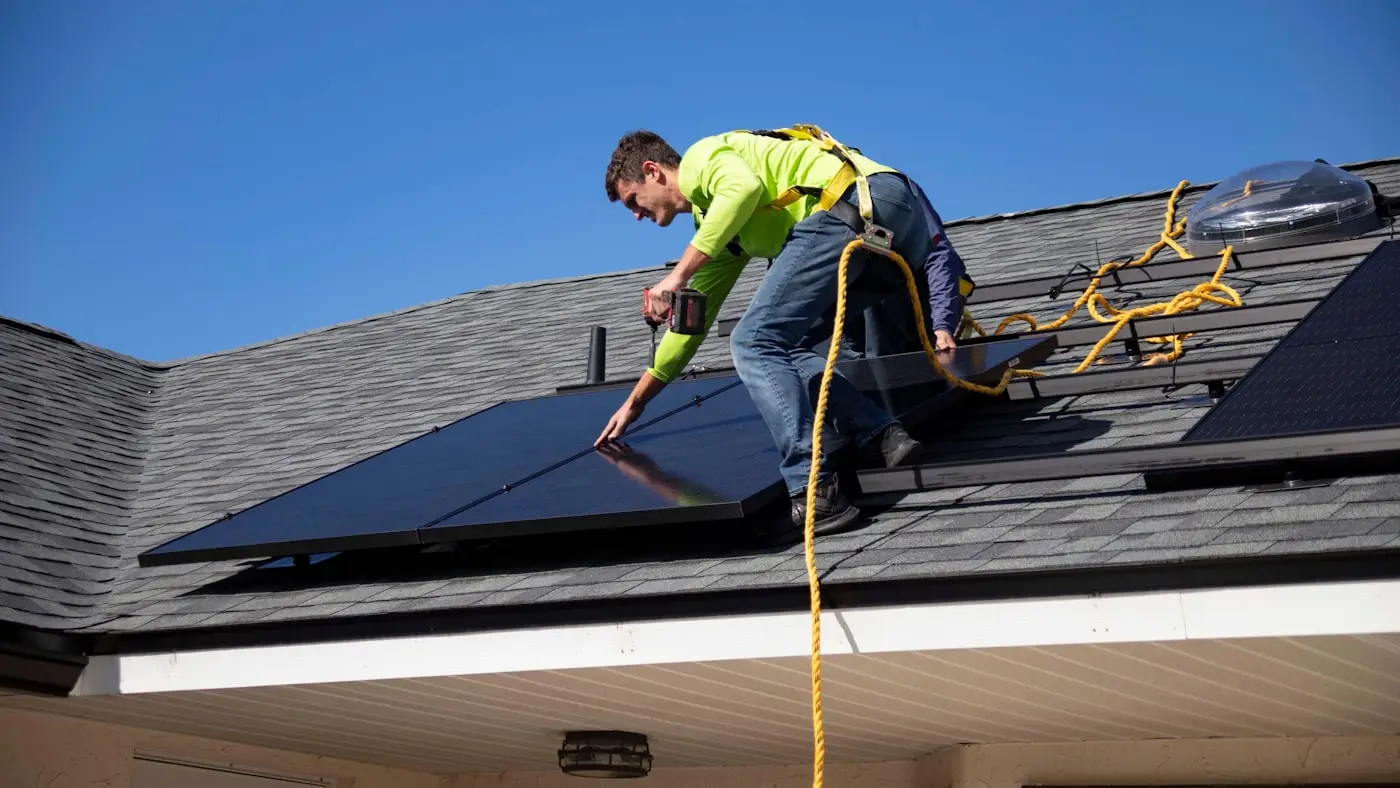 A solar installer fastening a panel to a residential shingle roof