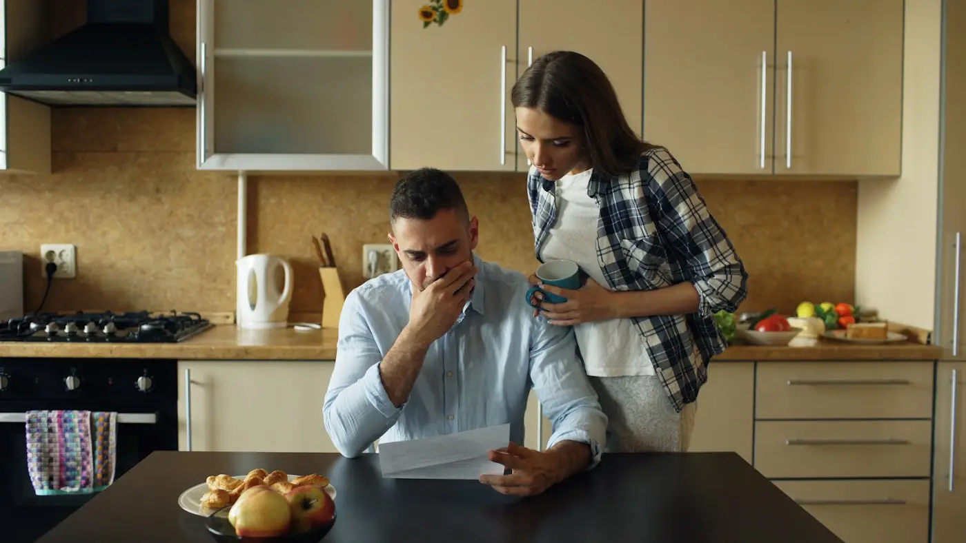 A couple at a kitchen table reading a letter with concerned expressions